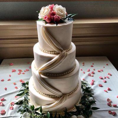 An elegant wedding cake with fresh flowers and greenery, surrounded with rose petals-oh so romantic!