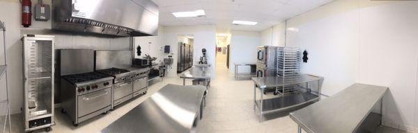 Main kitchen space with 5 prep tables, gas burners, conventional ovens, convection ovens, deli slicer, microwave, proofing cabinet.