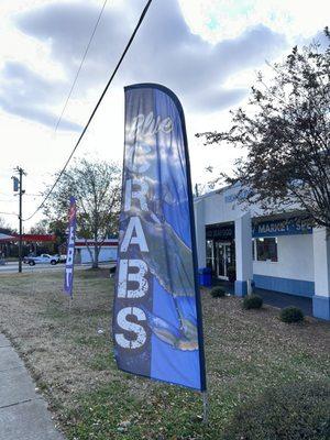 An outdoor flag sign advertising an offering of seafood (crabs) in front of at Forsyth Seafood Market and Café.