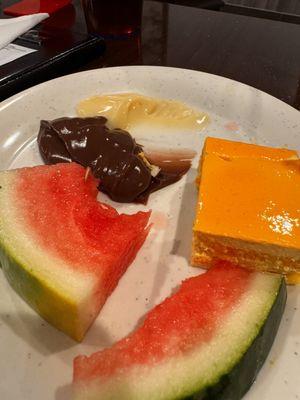 Half eaten water melon, half eaten snack pack jellos, orange fluffy cake.