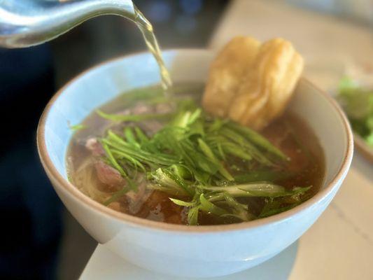 Hanoi Pho: a twist on the traditional pho with sliced ribeye, scallions, thai chili and a fried doughnut. The broth is spicy and delicious!