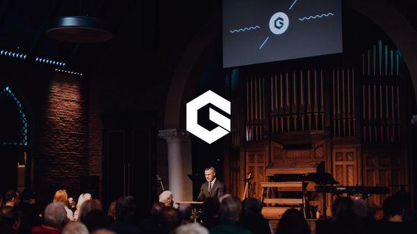 GracePointe's logo over top a picture of the founding pastor preaching.