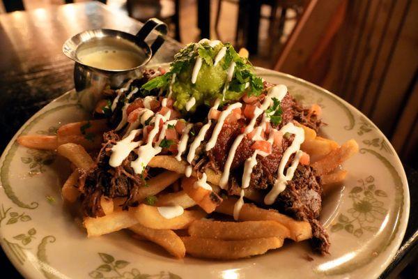 Loaded Birria Fries: french fries, shredded cheese, braised beef, salsa roja, crema guacamole, pico de gallo, Kavas Queso ($18).