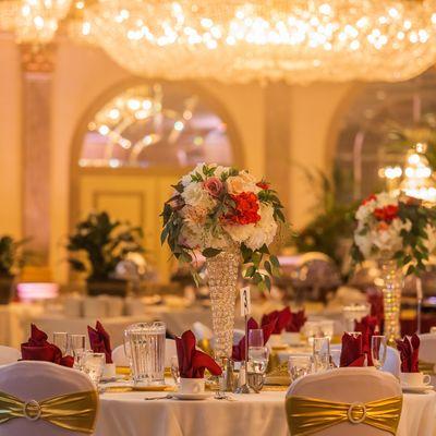 Wedding decor with white chair covers and gold sashes and burgundy accents.