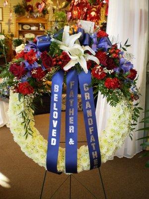 Red, White and Blue Sympathy Wreath of White Cushion Poms with Red Roses, Carnations & Hypericum, Blue Iris, White Orientals out top.