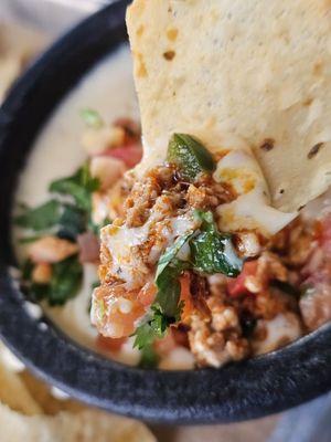 A Chip scooping a part of the Choriqueso dip.