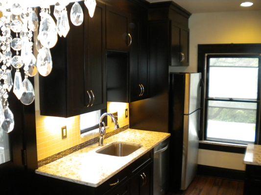 Sink wall showing quartz top, dark wood Shaker cabinets and tile and glass back splash.