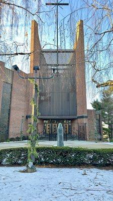 Looking at the front gates of the church with a spacial angle so that the bell's tower and cross can be seen.