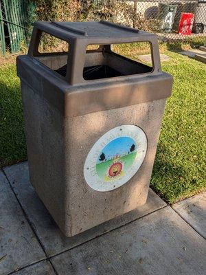 Trash can with a faded City of Hawaiian Gardens logo