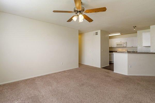 Living room with carpet flooring, multi speed ceiling fan, and kitchen in the background