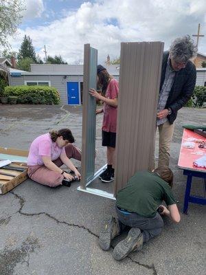 Middle school students and the head of school build a new shed for the playground