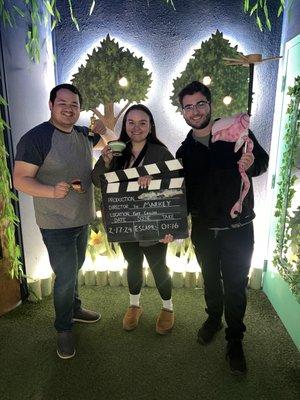 3 friends holding a half tea cup and mini trophy for escaping, clapperboard with date and time left to escaped, and a golf club w/ flamingo