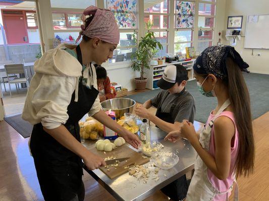 Adolescent students help elementary students prepare hot lunch.