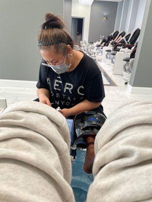 Lady doing pedicure & woman in back laid out on chair talking on phone.