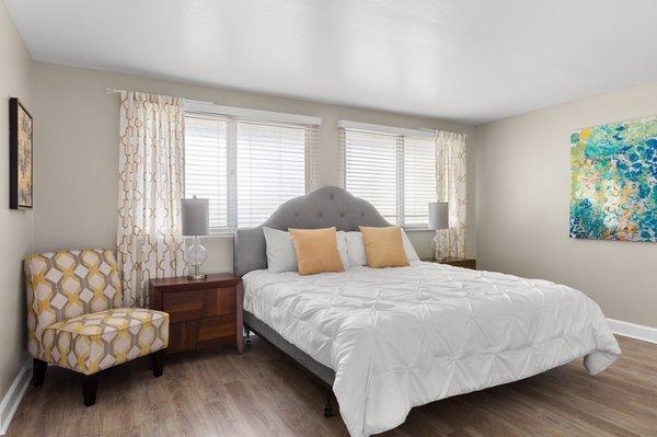 bedroom model showing queen size bed additional seating chair and 2 large windows