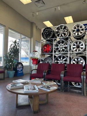 A display of rims in the waiting area, comfortable chairs, a TV not in this photo, magazines on a center table