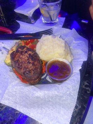 filet mignon and garlic mashed on a plastic plate on top of parchment paper that ripped when she cut the steak