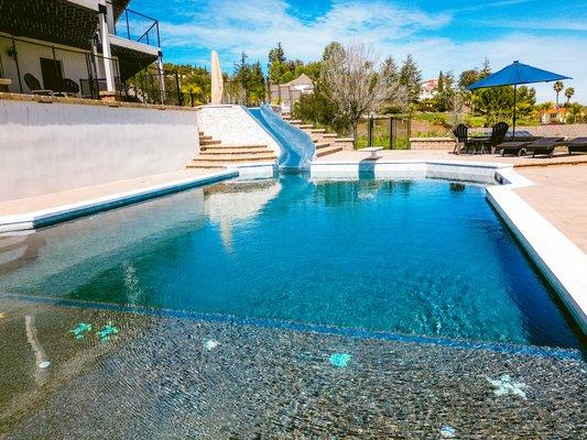 Baja Shelf with custom mosaic tile inlays, diving board, slide w/ 1x1 iridescent tiles, spa, outdoor kitchen, built-in firepit.