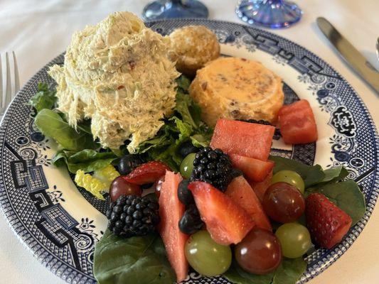 Chicken salad platter with fresh fruit,  a small orange gelatin,  and a mini lemon poppyseed muffin.