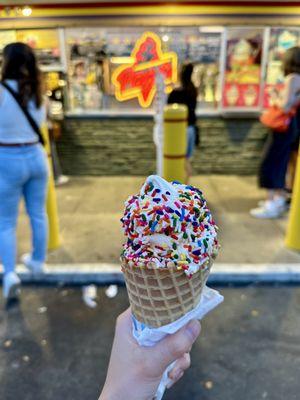 Vanilla soft serve with rainbow jimmies in a waffle cone