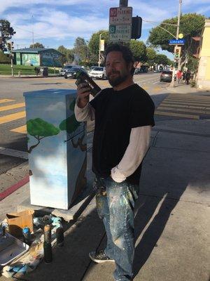 Sel (@Sel_Dog) painting a utility box Catty corner from the school. Matches the building behind him.