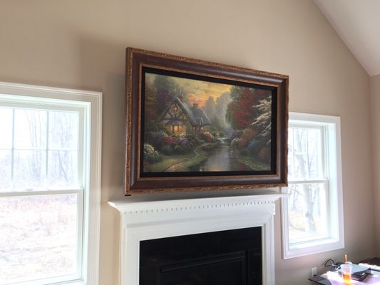 50" TV mounted above fireplace inside motorized picture frame w/ wiring concealed