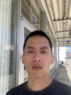 A former San Bruno local (whose mother tells him he's very handsome with his new haircut) takes a selfie in front of a random storefront