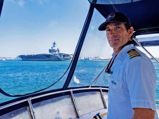 One of our captains with an aircraft carrier in the background. There are many things to see on San Diego Bay while on a yacht charter.