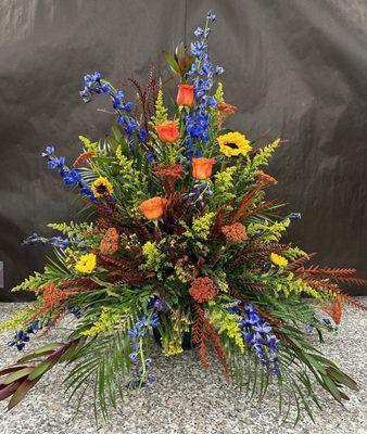 Stunning arrangement featuring blue delphiniums, vibrant orange roses, and cheerful sunflowers.