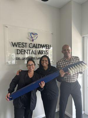 An Image of CEO Dr. Jayshree Sawhney and two of her employees posing with a giant toothbrush