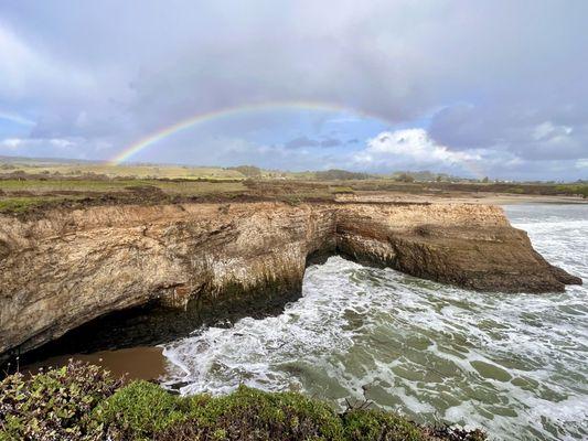 Rainbow over the cliff, grotto and ocean