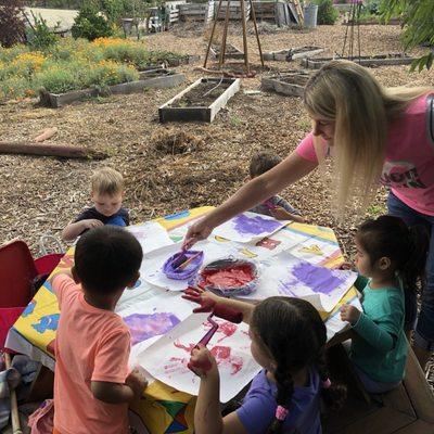 Miss C helping the toddler class paint in the Community Garden.