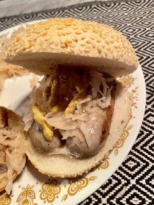 Kielbasa on sesame kaiser roll with brown mustard and sauerkraut.