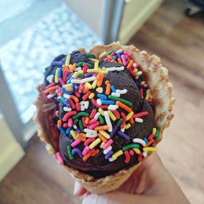 Vegan dark chocolate coconut ice cream with rainbow sprinkles in a sugar cone