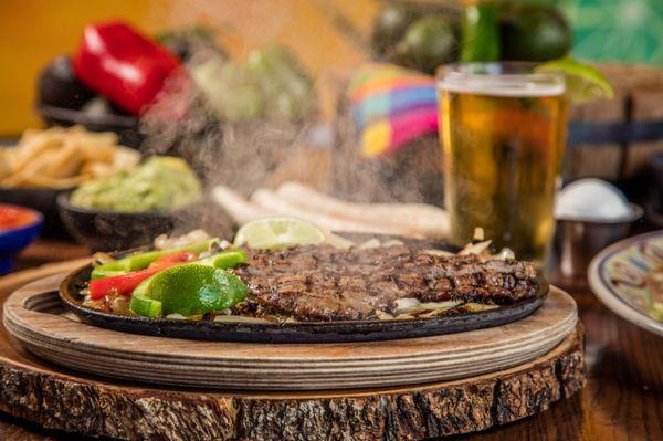 Beef fajitas - served sizzling hot on a bed of sautéed onions and bell peppers, w/ refried beans, rice