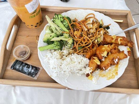 Orange chicken with little pieces of a fresh slice of orange on top, broccoli in garlic sauce, white rice, and veggie lo neon noodles.