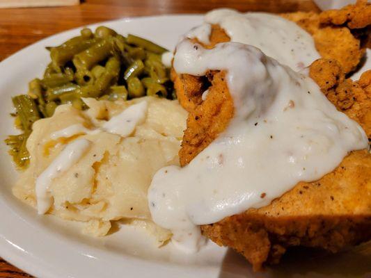 Chicken fried chicken  with mashed potatoes, white gravy, and green beans.