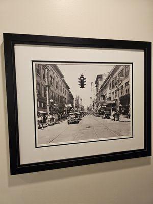 An old black and white framed photograph of the street where this store is located, many years ago.