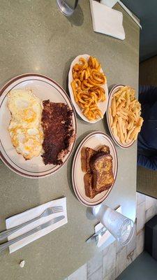 Corned beef hash and eggs with curly fries, challah French toast, and mushroom cheese omelette with fries