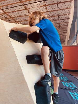 boy in blue shirt climbing up black climbing holds