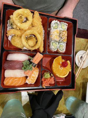 Bento box with tempura vegetables and fish sushi and sushi rolls and fruit slices