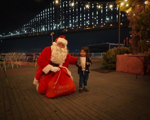 Santa on the Embarcadero with Bay Bridge in background by local SF company. Hire Santa from Holiday of Wonders