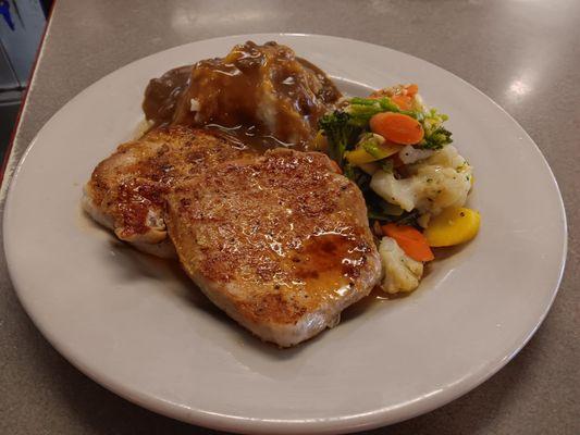 Pork chops served with mashed potatoes, vegetables and beef gravy.