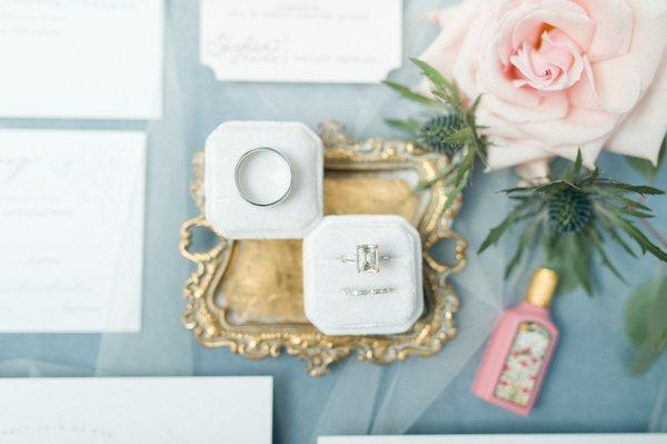 Wedding detail photos of wedding bands in a white velvet ring box with a blue background