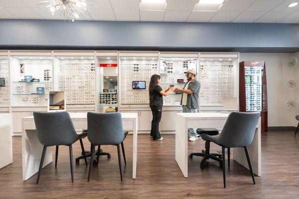 An optician assisting a patient in a modern showroom with numerous eyewear options at Custom Eyes Optometry, Costa Mesa, CA.