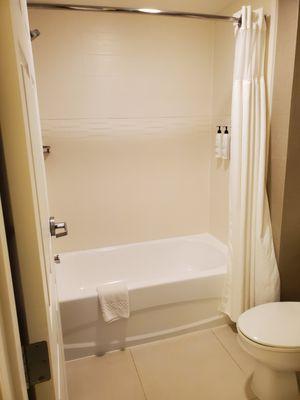 Bathtub with shower. Bottles on the wall with body wash, shampoo, and conditioner.