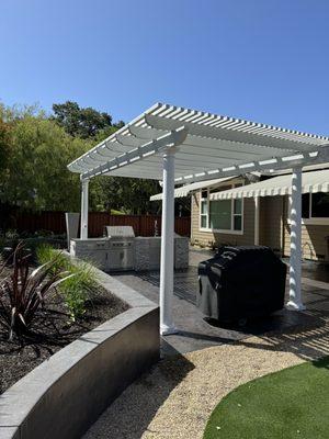 Smooth finish colored retaining wall & stamped patio, turf, planting, outdoor kitchen & pergola.