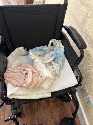 A wheelchair with a soiled diaper next to unused diapers in my family members room.