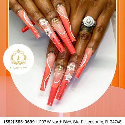 Elegance at your fingertips with this vibrant orange nail design and delicate white floral accents