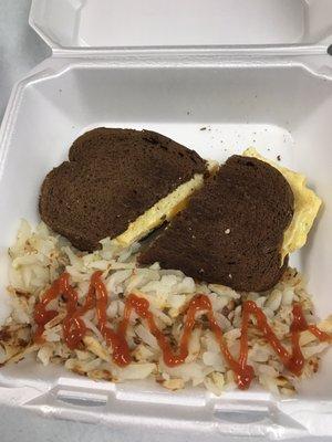 Egg and cheese on rye breakfast sandwich with a side of hash browns.